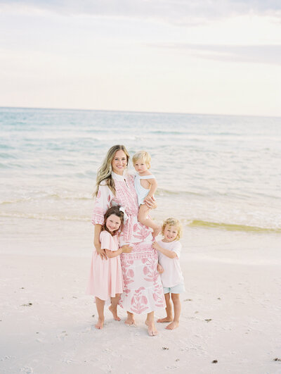 Mom and her three kids standing on the beach with ocean in the background