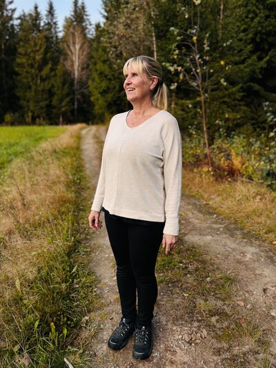 Kotihoitaja MaaRia hymyilee ulkona ja seisoo pellon reunassa