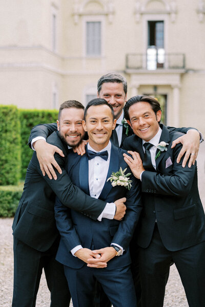 Joyful groom surrounded by his groomsmen in elegant suits during a wedding day portrait, captured in a candid moment