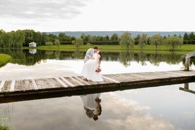 A wedding couple standing on a rock overlooking a lake.