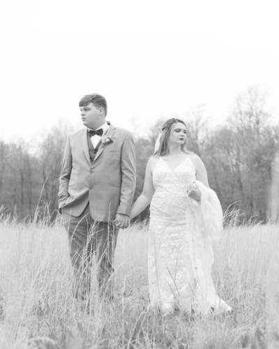 Groom and bride hold hands while standing in a field