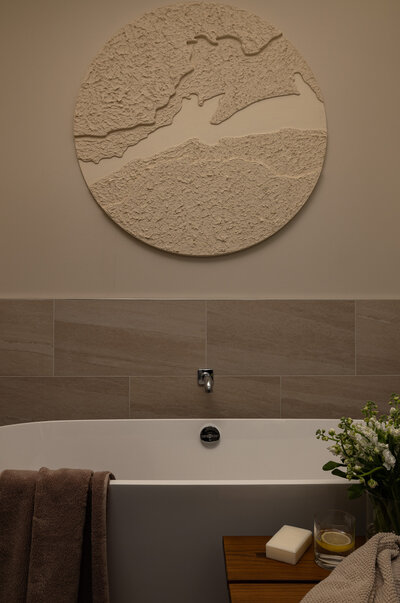 Vertical shot of a freestanding tub in front of textured stone walls with artwork and decor in a primary bathroom at the Grand Hyatt in Park City, designed by Sister Studio.