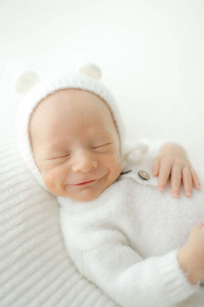 adorable newborn baby boy smiling as he dreams with dimples wearing a handmade hat by an okc grandmother