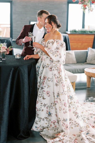 Bride in off-the-shoulder floral wedding dress and groom toasting with champagne during their luxury wedding reception at the Kimpton Armory.