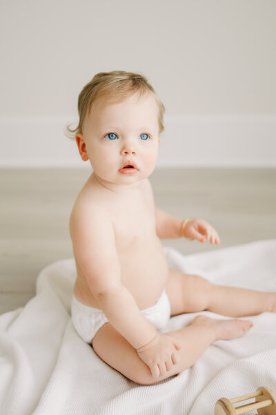 One year old baby girl in diaper cover plays during studio session with Worth Capturing Photography