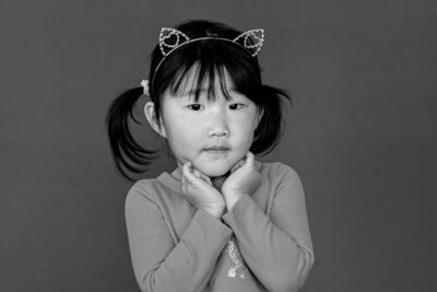 Girl wearing a cute cat ear headband and her hands uder her chin, with a minimal smile she poses for her school photo