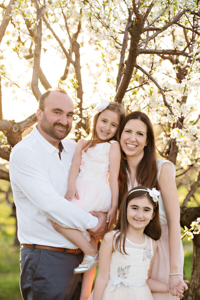 mom and dad with their two daughters for their Burlington Photographer white cherry blossom photography session.