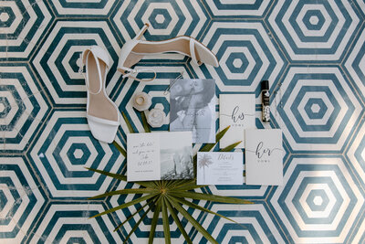 Mexico wedding details flatlay with vow books, shoes, rings, and palm leaves on patterned tile at Acre Resort.