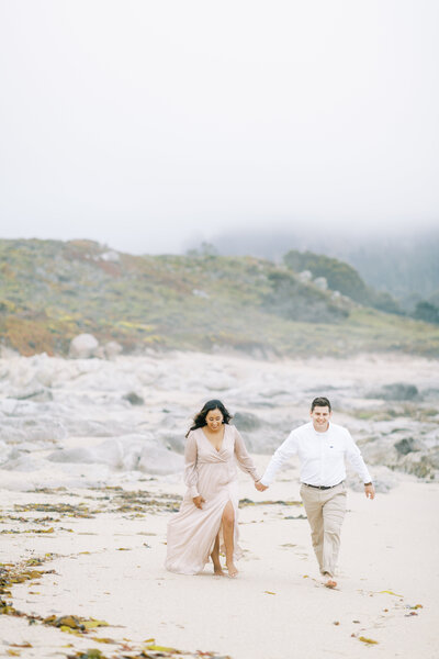 engaged couple holding hands walking along beach in carmel