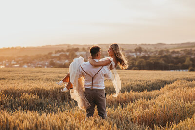 groom carries his wife through field of wheat