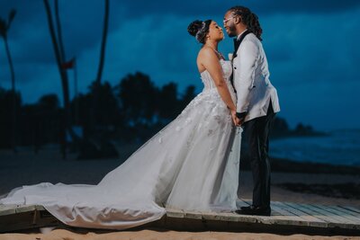 A bride and groom standing on a dock at night.
