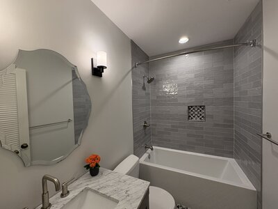 A remodeled bathroom featuring gray wall tile, patterned floor tile, a modern vanity, and a white tub-shower combination.