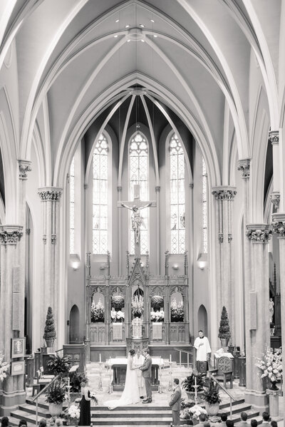 A wide, B&W photo in a catholic church wiht the bride and groom exchanging vows in Huron, Ohio