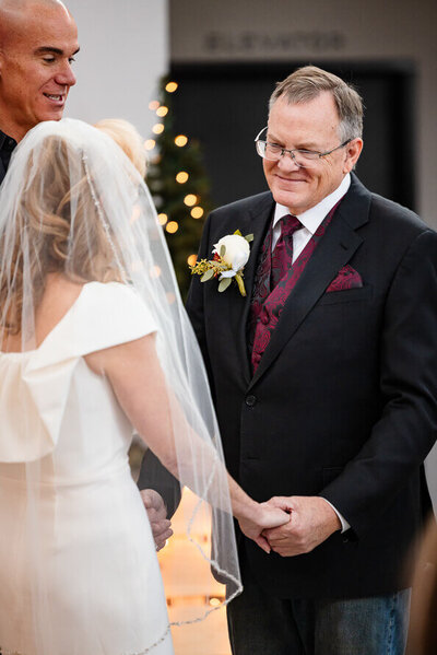 Older man in a suit smiles at his new bride during their wedding.