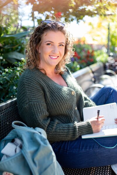 Samantha Burmeister sitting on a park bench, writing in a notebook.