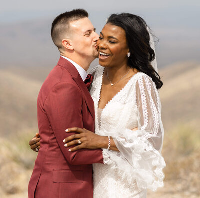 couple laughing and smiling at each other during their adventure session on a mountain top