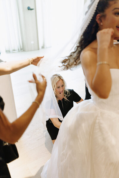 Female wedding planner helping bridesmaid arrange pink dress