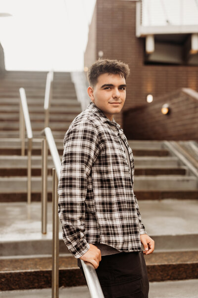 HIgh school boy stands with his back against a metal stair rail in Downtown Denver for his urban 