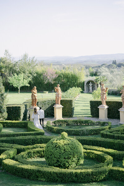 Bride and groom walk together facing away from the camera in the garden at Villa Catignano in Tuscany, shot by Nathan Shute Photography