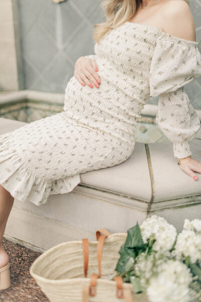 Expecting mother in a floral dress sits near a Kansas City fountain, captured during a serene outdoor maternity session.