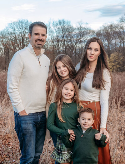 Professional family portrait by Stamford CT photographer featuring parents with three children in coordinated green and cream fall colors in natural outdoor setting
