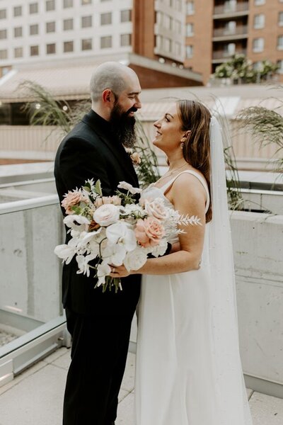 In this romantic photo, the bride and groom share an intimate moment on the rooftop, gazing lovingly at each other as they lean in for a kiss. Surrounded by a stunning backdrop, their soft earth-toned bouquet complements the atmosphere perfectly. This enchanting scene captures the essence of their love story, ideal for couples planning a wedding in Ottawa seeking inspiration for their special day.
