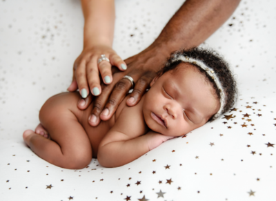 Baby with mom and dad holding her back while sleeping on a white cloth with stars