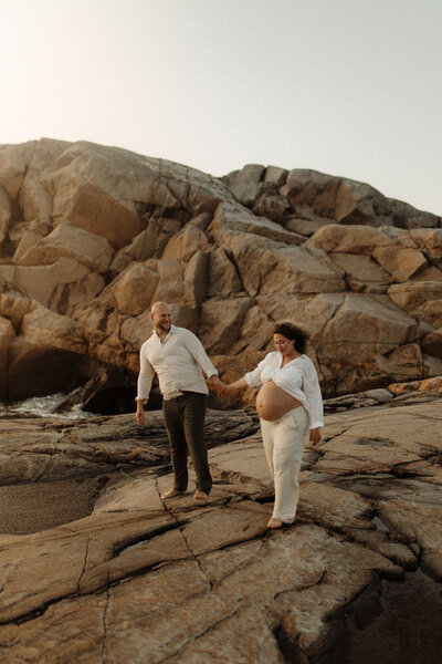 en gravid kvinna och hennes man går barfota över klippor
