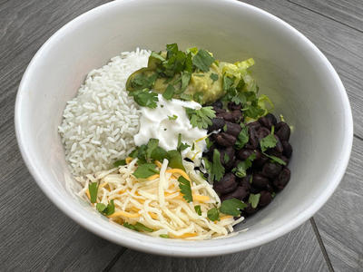 Smartphone displaying the Supper Club meal planning app with weekly menus, next to fresh produce spilling from a grocery bag.