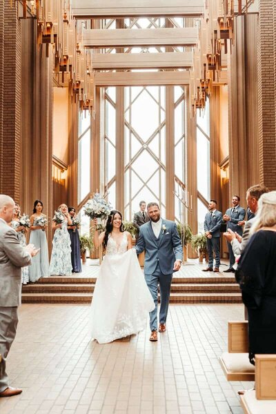 Bride and groom walk hand in hand down the aisle at Marty Leonard Chapel–captured by a Texas wedding photographer.