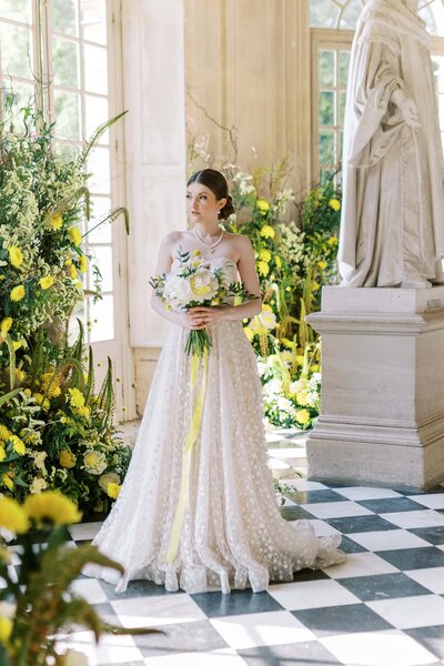 A styled woman is standing in front of a marble statue