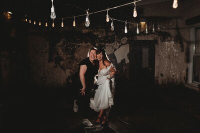 wedding photographer posed with bride under string lights