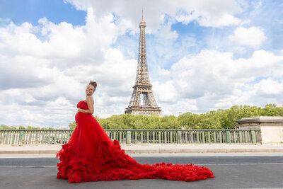 Pregnant woman in red princess gown during maternity photoshoot at Bir Hakeim bridge with Eiffel Tower view