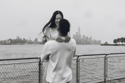Engaged couple spinning on a pier with New York City skyline in the background