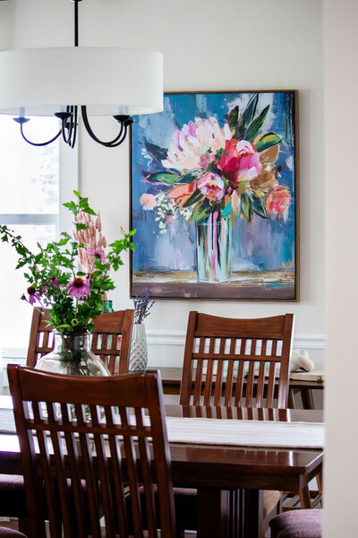 Dark wooden dining room table and chairs with wildflowers in vase and floral canvas artwork
