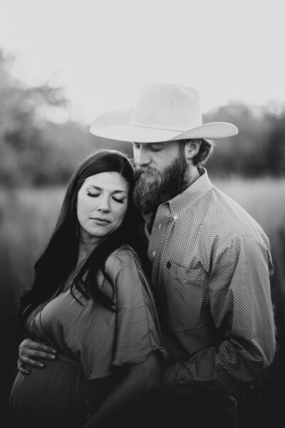New parents sitting in a field of tall golden grass admiring their newborn baby girl. 