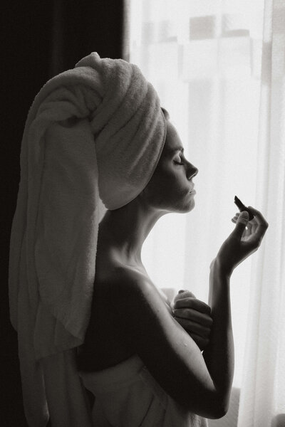 woman with a towel in her hair putting on lipstick