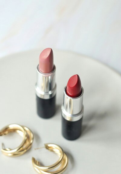 Two tubes of lipstick sitting next to gold hoop earrings