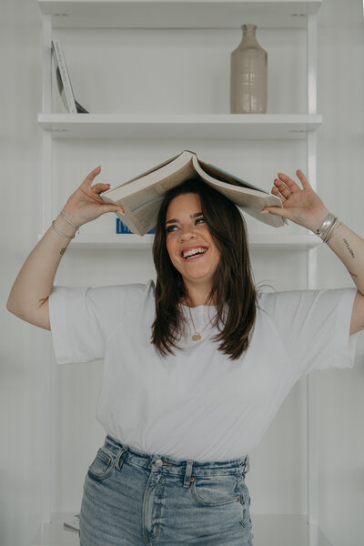 Sara Noel Website & Launch Copywriting at Between The Lines Copy holding book over her head and smiling.