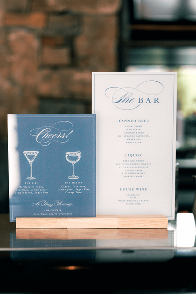 Custom acrylic bar menu for a pastel wedding at Moonlight Basin, featuring signature cocktails named after the couple, printed in blue and white with elegant typography.