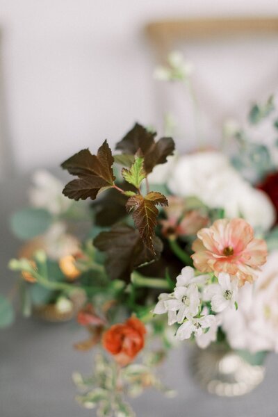 A close up of a flower arrangement with peach, red, white and brown flowers.
