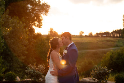 Ohio couple kiss and embrace one another during a golden hour sunset in Ohio on their wedding day. Photo taken by Aaron Aldhizer