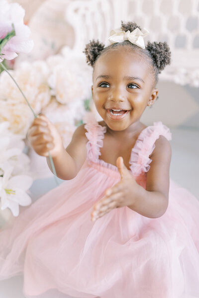 Little girl in a pink dress smiling and holding a flower