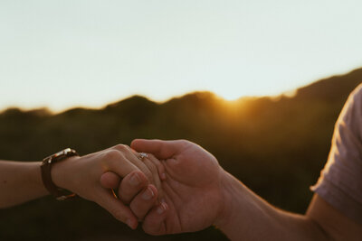 Couple holding hands with wedding ring in view during a sunset at Pensacola Beach in Florida