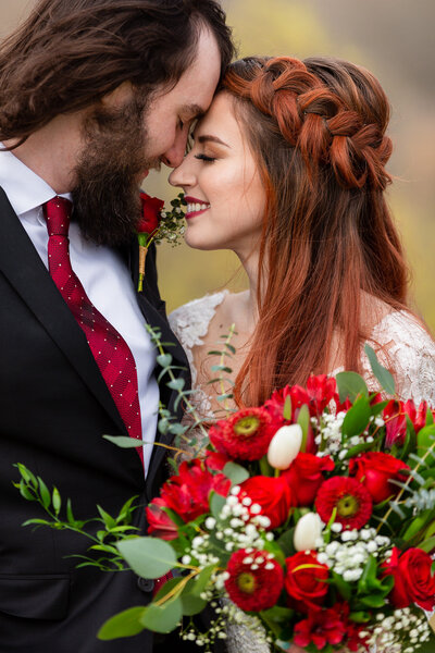 Red haired bride and groom forehead to forehead  smiling together with eyes closed with red flower bouquet with Dallas wedding photographer Stefani Ciotti Photography
