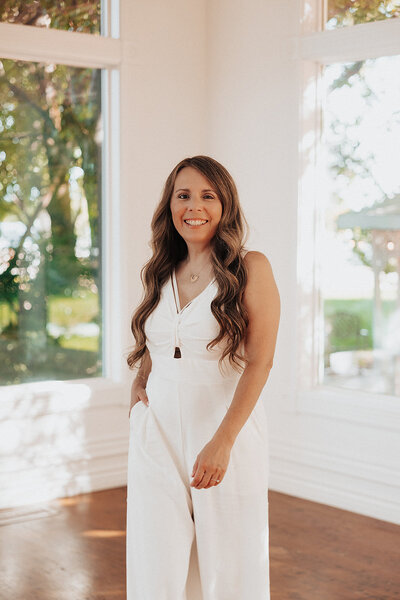Patty dressed in white standing in front of windows smiling at the camera
