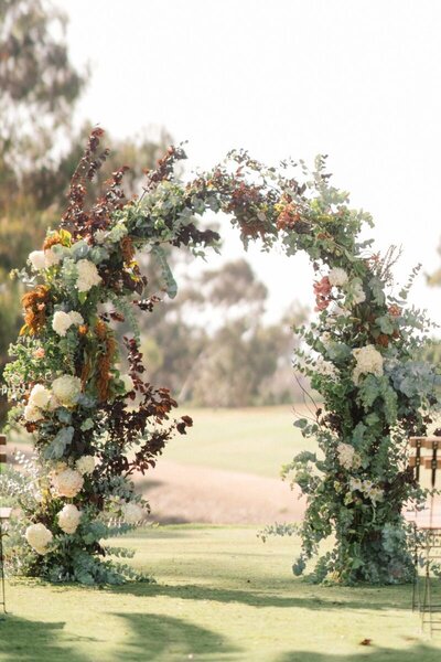 Fall arch flowers with burnt orange and deep red by Kendra’s Events at Diamond H3 Ranch wedding. in Weatherford, Texas