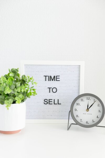 White letter board that days Time To Sell with office plant and time clock