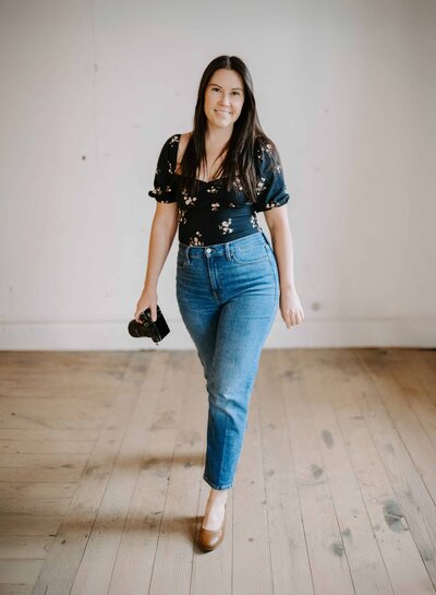 Photographer walking confidently in a bright studio space with camera in hand, smiling warmly.