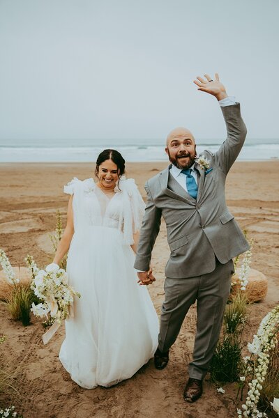 man and woman cheer as they walk down a sand coverisle on the Oregon coast